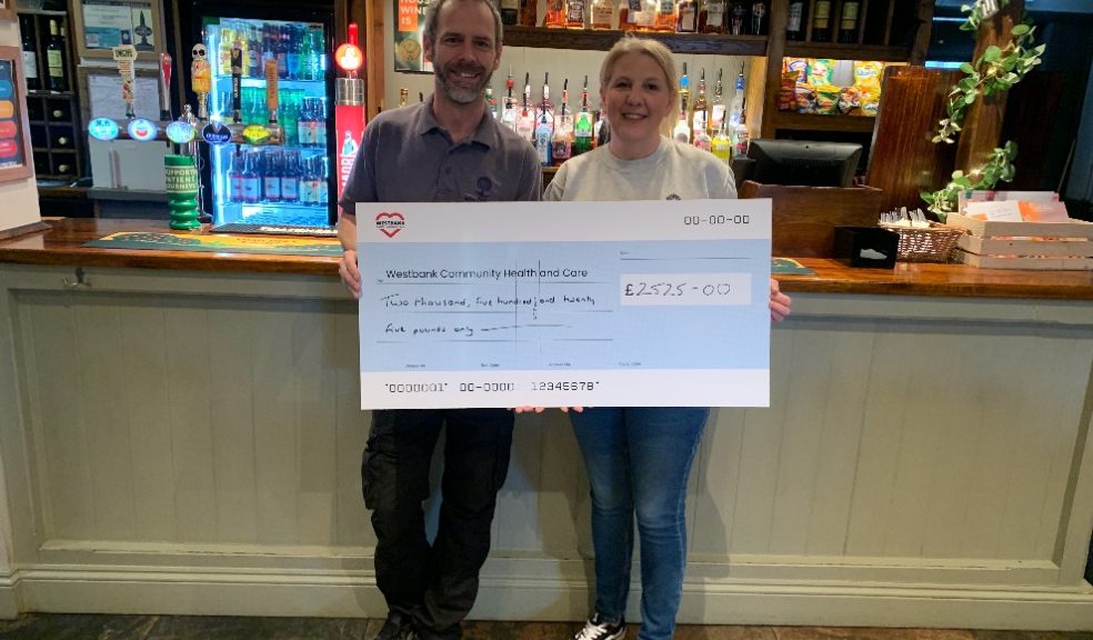 photo of man and woman holding a fundraising cheque in front of a pub bar